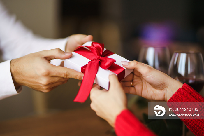 Man gives to his woman a gift box with red ribbon. Hands of man gives surprise gift box for girl. Yo