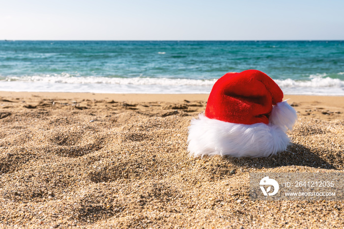 Santa Claus hat on sandy beach. Creative Christmas or New Year concept.