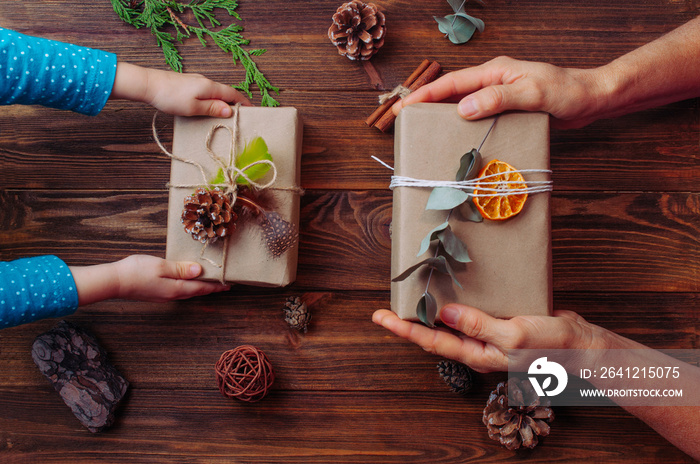 Kids and grandmother hands holding Christmas gift boxes decorated with natural details