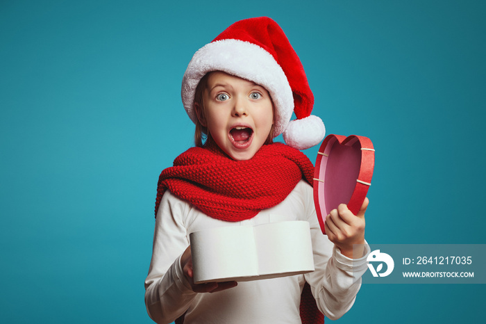 惊讶的可爱小女孩戴着圣诞帽和红围巾，独自拿着打开的礼物盒