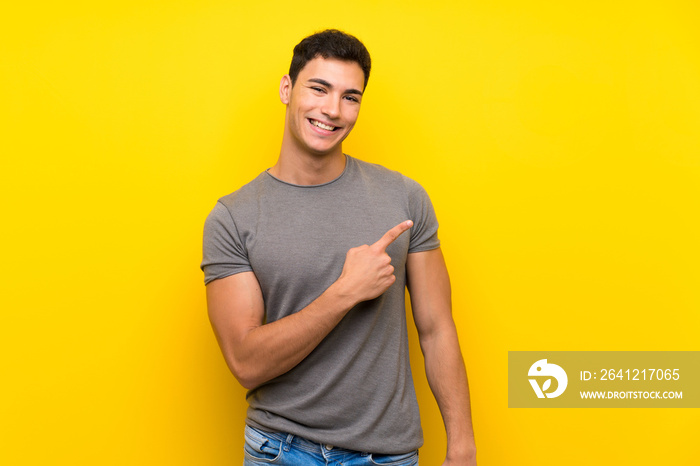 Handsome man over isolated yellow wall pointing to the side to present a product