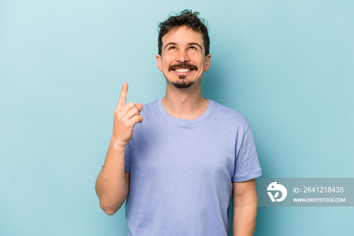 Young caucasian man isolated on blue background indicates with both fore fingers up showing a blank 