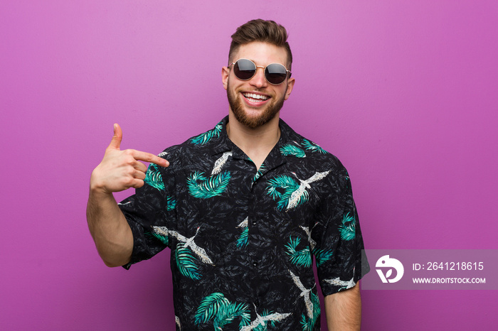 Young man wearing a vacation look person pointing by hand to a shirt copy space, proud and confident