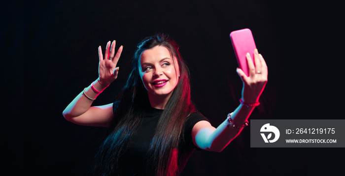 Tik tok advertisement concept. Young girl posing with smart phone in her hands, making selfie on bla