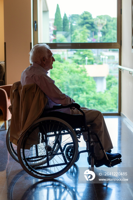 Solitary old man in wheelchair against back lit window.