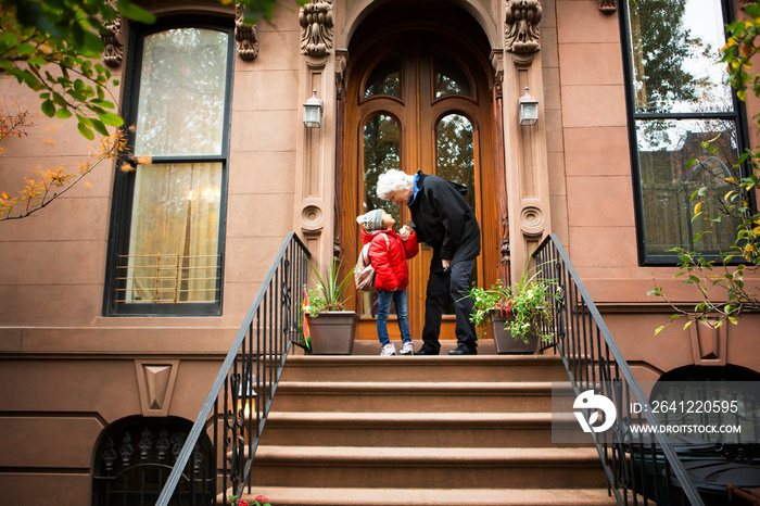 Grandmother with granddaughter (4-5) standing in front of house