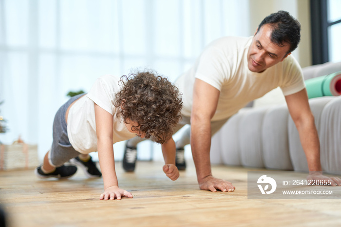 在家训练。运动型的拉丁中年父亲一边教儿子做俯卧撑，一边花钱