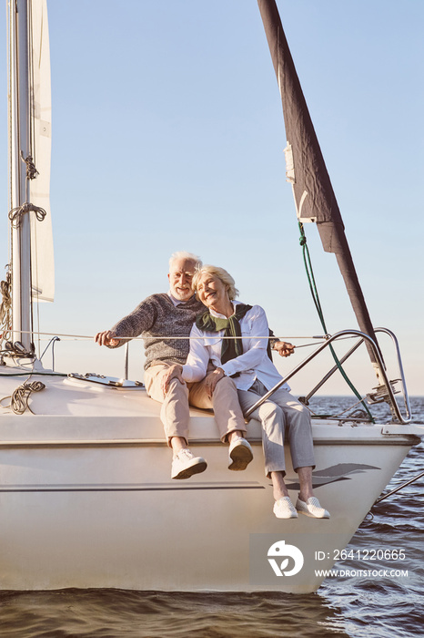 Happy senior couple sitting on the side of sail boat or yacht deck floating in sea. Man and woman en