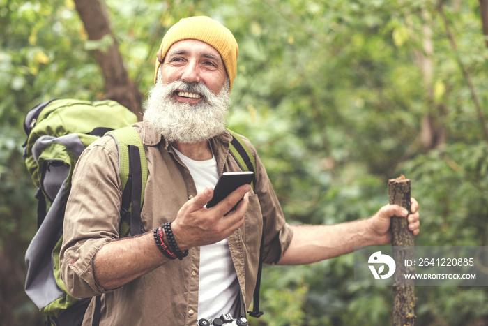 快乐的老人带着智能手机导航仪在林地徒步旅行