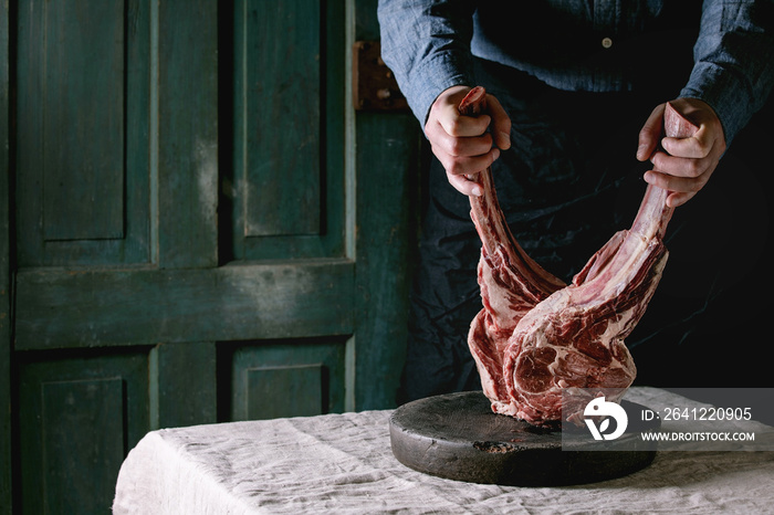 Mans hands holding raw uncooked black angus beef tomahawk steaks on bones on linen table cloth. Rus