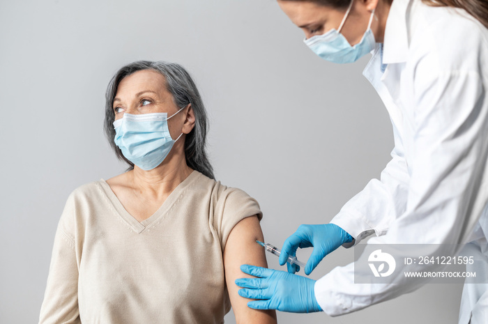 An elderly woman getting a vaccine for coronavirus, a doctor wearing mask and gloves with a syringe 