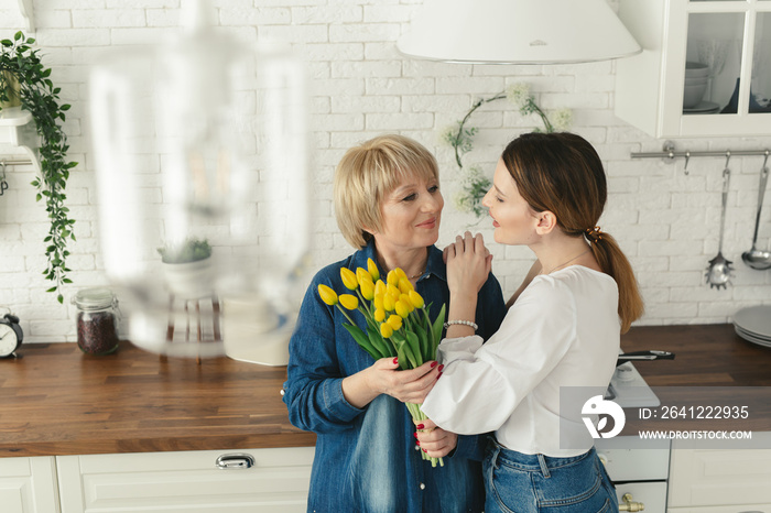 Beautiful adult woman is giving flowers to her mature mother. Womens day