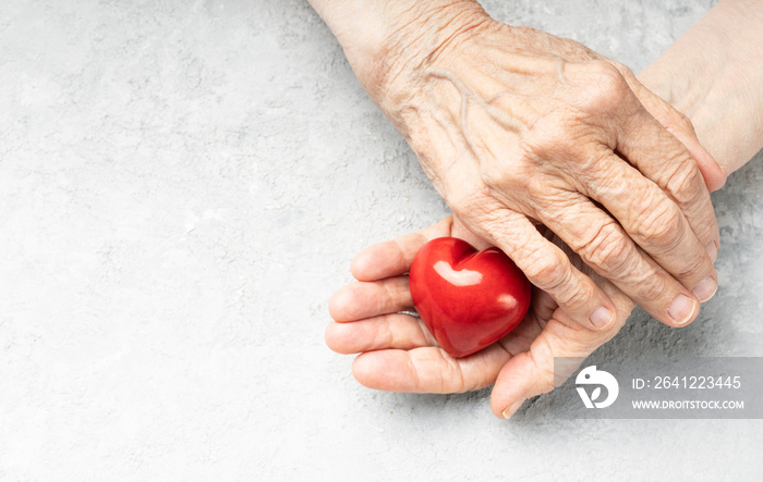 Elderly heart health. Wrinkled hands holding red heart symbol. Background with copy space.