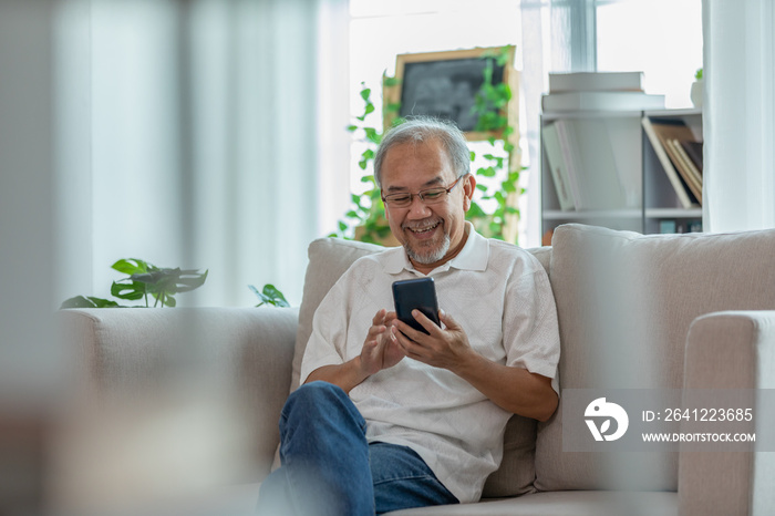 幸福的亚洲老人坐在沙发上用手机和社交媒体在家微笑，老人