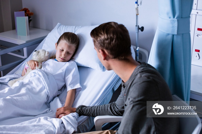 Father sitting beside her daughter lying on a hospital bed