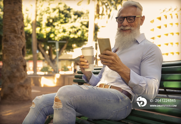 时髦的老年男子在公园里使用智能手机应用程序喝咖啡。成熟的时尚男性有f