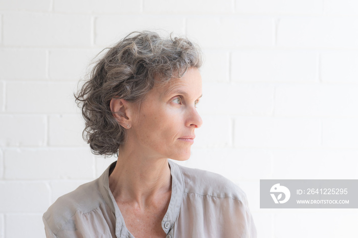 Side view of natural looking middle aged woman in silk shirt against white background (selective foc