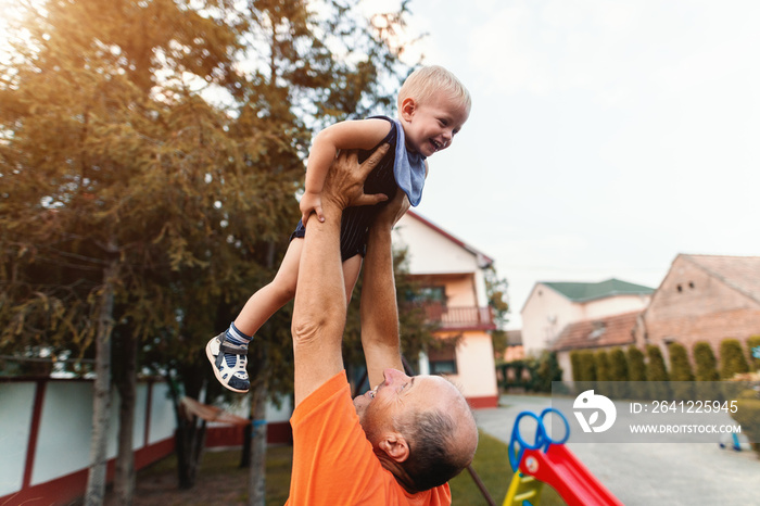 Grandfather lifting up his grandson and playing with him. Countryside exterior.