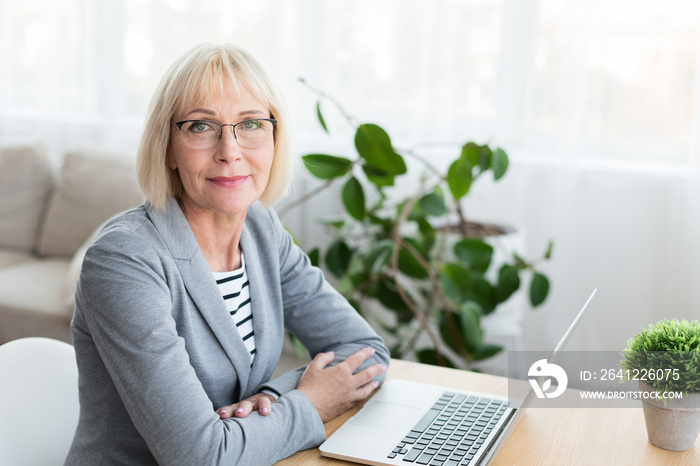 Senior woman working on laptop, looking at camera