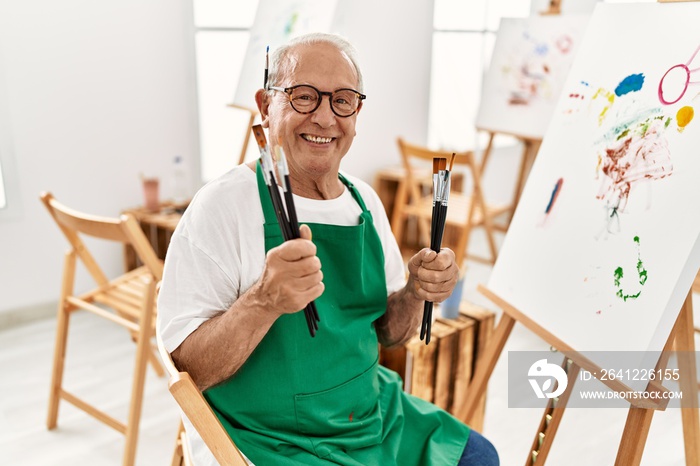 一位头发花白的资深艺术家在艺术工作室拿着画笔微笑着。