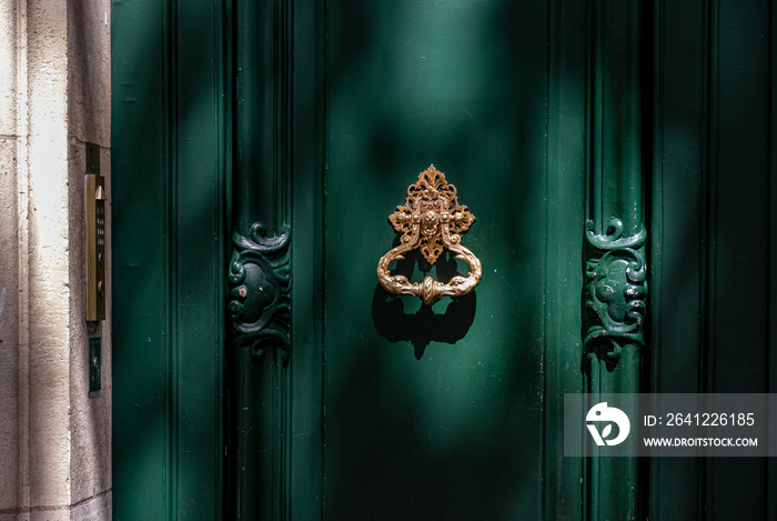 Old door with knocker. Green painted wooden framed door with gorgeous antique ornate knocker and car