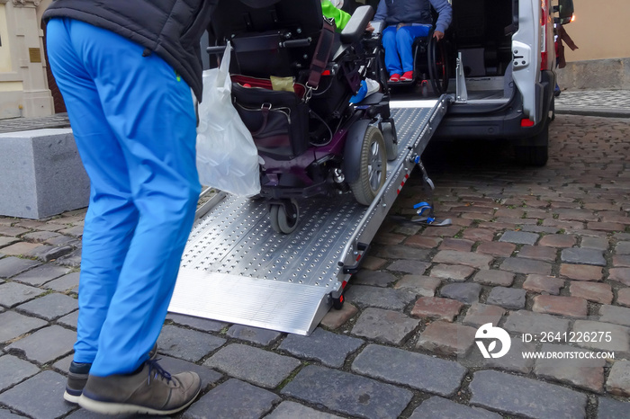 Assistant helping disabled person on wheelchair with transport using accessible van ramp