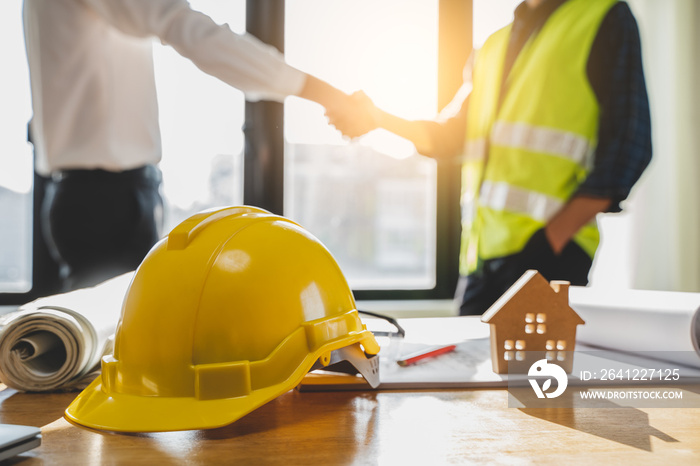 Close up yellow safety helmet on the table and contractor and customer shaking hands after confirm t