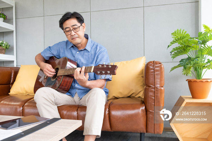 Asian elder man enjoy playing guitar at the sofa inside of well interior decoration house. Active se
