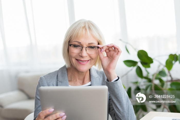 Elderly woman browsing on digital tablet, reading news