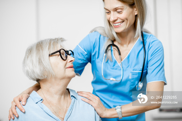 Nurse taking care of senior woman, hugging her shoulders in the clinic or home for elderly