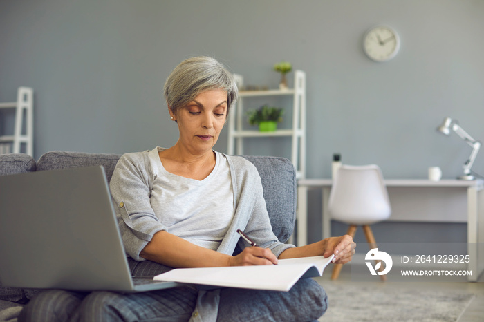 Senior woman making notes during online lesson on laptop at home