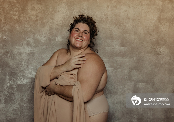 portrait of a plus size woman with curly hair looking up and smiling with hugging self