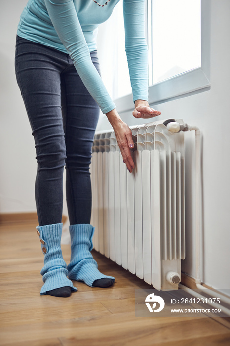 Woman heating her hands on the radiator during cold winter days.