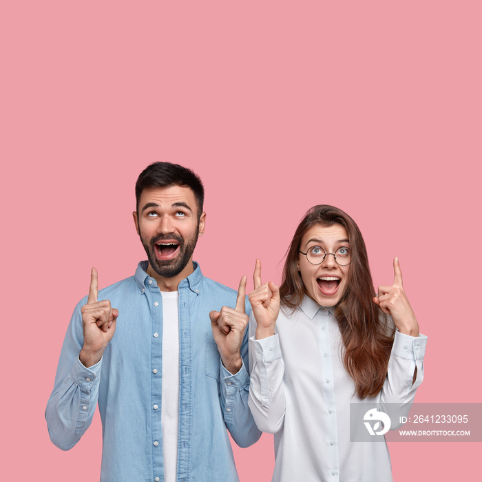 Young happy couple points at blank copyspace above, advertise great product, opens mouthes from plea