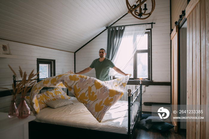 A young man makes a bed in a cozy bedroom at home.