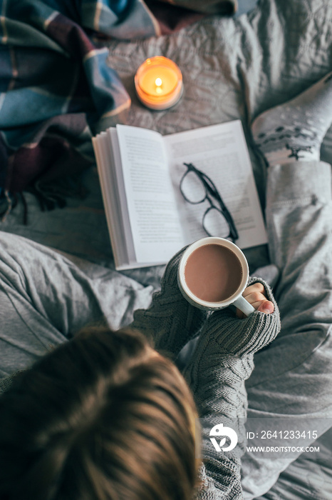 Young girl drinking hot chocolate on cozy bed. Concept of autumn or winter weekend, top view