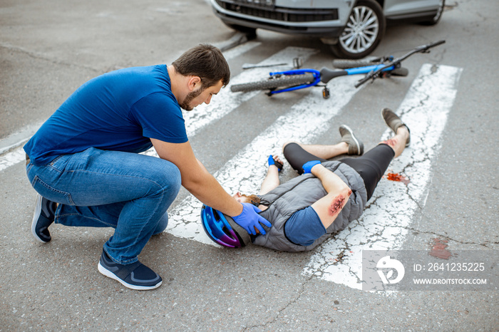 Road accident with injured cyclist on the pedestrian crossing with passerby pedestrian providing fir