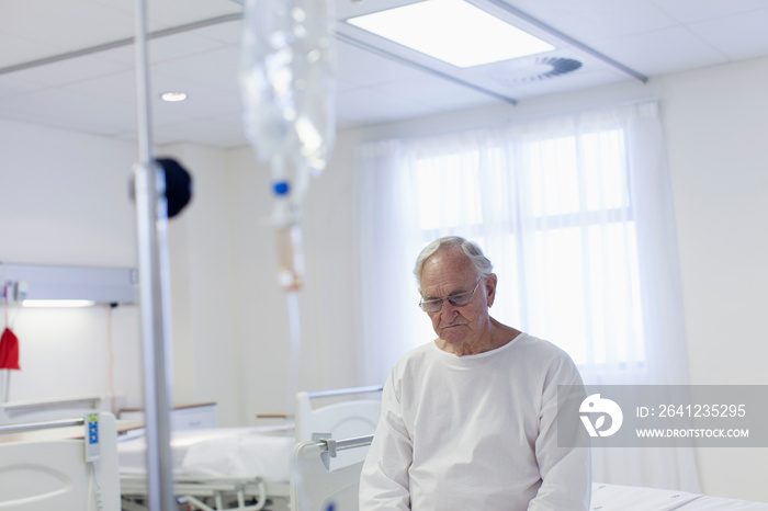 Worried male senior patient sitting on edge of hospital bed