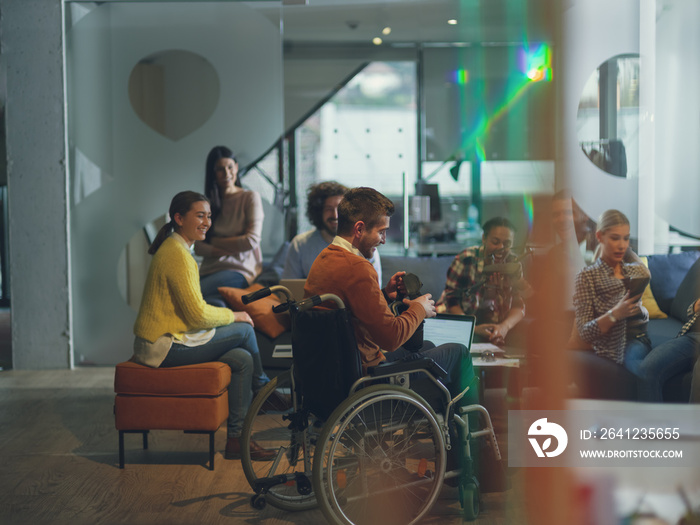 Disabled businessman in a wheelchair at work in modern open space coworking office with team using v