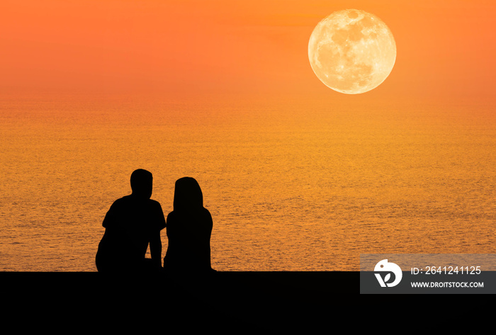 silhoutte后视浪漫情侣坐在日落时分的海滩上放松，满月