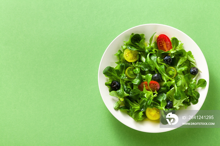 fresh salad of arugula and valerian leaves with colored tomatoes and blueberries in a plate on a gre