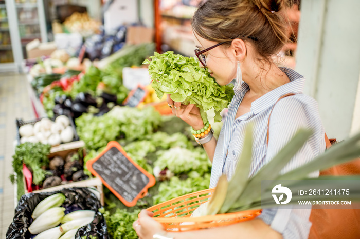 法国菜市场上，一位年轻女士拿着篮子站着挑选新鲜沙拉