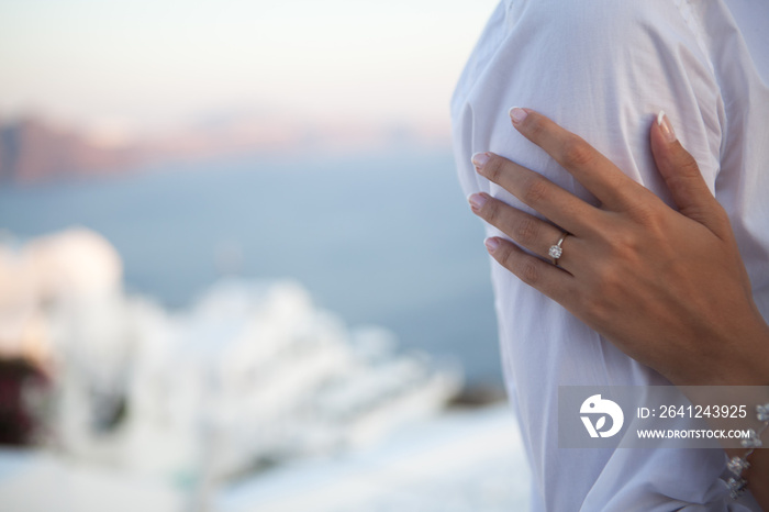 Close-up of a female hand with a wedding ring hugging her husbands hand over of a blurred sea and sk