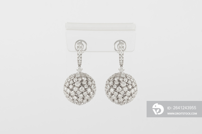 Pair of white golden diamond earrings on transparent stand. Golden earrings with diamonds, luxury je