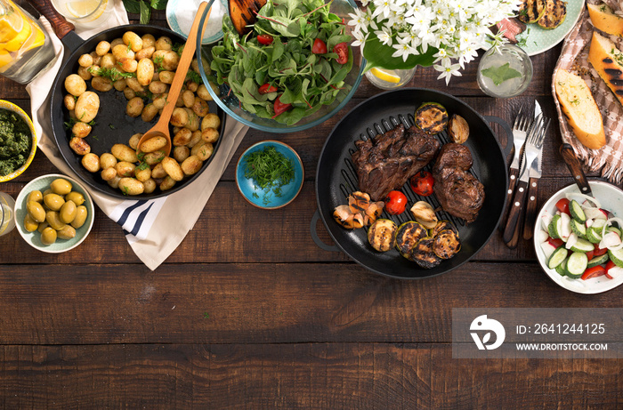 Grilled steak, vegetables, potatoes, salad, snacks, lemonade on wooden table