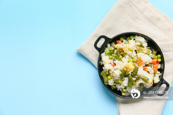 Frying pan with cooked vegetables and rice on color background