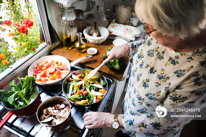 Elderly woman cooking healthy couscous and vegetables in a pan