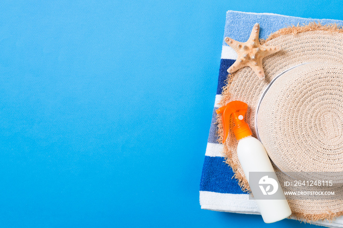 Summer beach flat lay accessories. Sunscreen bottle cream, straw hat, towel and seashells on colored