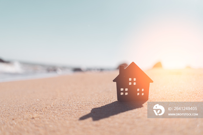 Small home model on sunset beach sand texture background.