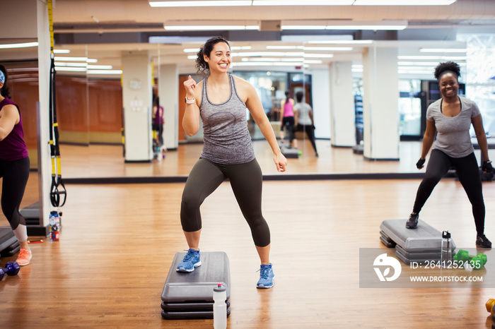 Smiling female athletes stepping on aerobics steps against mirror in gym